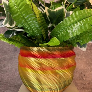 May include: A gold, red, and green swirl planter with a leafy green plant inside. The planter has a shiny, metallic finish.