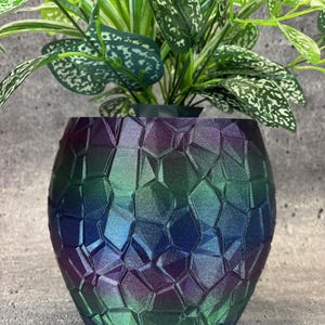 May include: A iridescent green, blue, and purple vase with a geometric pattern. The vase is made of a textured material and has a round shape.