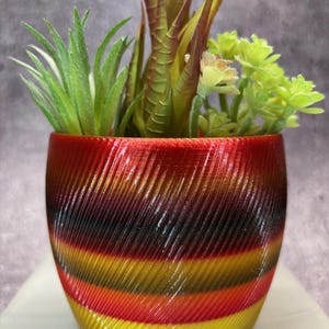 May include: A small, colourful, striped planter with a variety of green succulents. The planter is made of a 3D printed material and has a glossy finish.