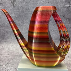 May include: A decorative watering can with a unique, curved design. The can features a gradient of colors, including red, orange, and yellow stripes. The handle has an open, lattice-like design. The spout is long and slender.