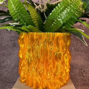 May include: A bright orange, textured, 3D printed planter with a leafy green plant inside.