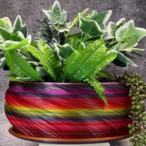 Op de afbeelding: Een kleurrijke, swirl-vormige keramische plantenpot met een houten basis. De pot is gevuld met groene bladplanten, waaronder varens en klimop.