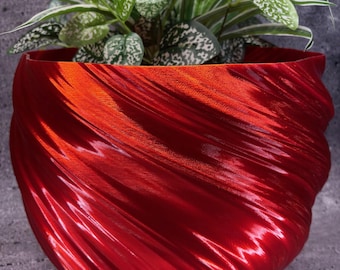 May include: A vibrant red, textured planter with a swirling design, holding a lush green plant with white-speckled leaves. The planter's glossy finish reflects light, creating a dynamic visual effect. The plant adds a natural element to the modern design.