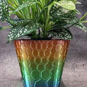 May include: A green, blue and orange plant pot with a honeycomb pattern. The pot is made of a textured material and has a wide base.