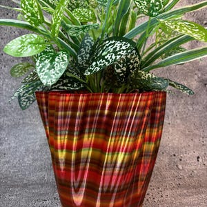 May include: A colorful, striped, 3D printed planter with a green plant with white speckles. The planter has a wavy, organic shape.