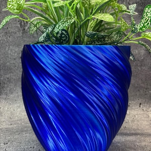 May include: A striking blue planter with a textured, swirling pattern, containing vibrant green plants. The planter's design and colour provide a contrast with the foliage, making it a decorative accent for any home or office. The planter is approximately 20 cm in height.