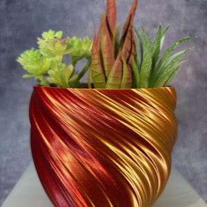 May include: A red and gold swirl planter with three succulent plants. The planter is made of a shiny, textured material.