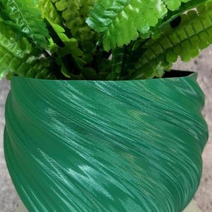 May include: A green, swirl-patterned plastic planter pot. The pot is made of a textured material and has a smooth, rounded shape.