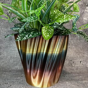 May include: A green plant with white speckles in a gold, brown, and black swirled ceramic planter.