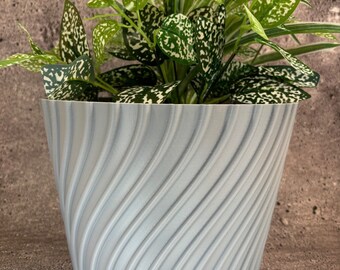 May include: A light gray planter with a swirl pattern. The planter is filled with a green plant with white speckles on the leaves.