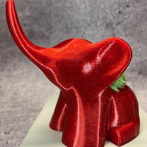 以下が含まれることがあります： 小さな多肉植物が入った赤い3Dプリントの象のプランター。プランターは光沢のあるテクスチャのある素材で作られています。