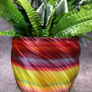 Może przedstawiać: Kolorowa, ceramiczna doniczka w paski i z wzorem spiralnym, z zieloną rośliną w środku.