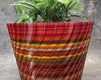 May include: A red, yellow, and green striped planter with a swirling pattern. The planter is filled with a green plant with white variegation.