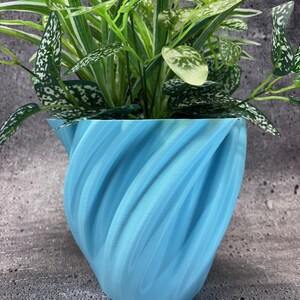May include: A light blue, swirl-shaped ceramic planter with a green plant inside.