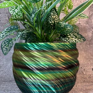 May include: A green and iridescent planter with a swirling pattern. The planter is made of a smooth, shiny material and has a round shape.
