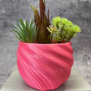 Peut inclure: Un pot de fleurs rose en forme de spirale avec une variété de succulentes artificielles vertes et brunes.