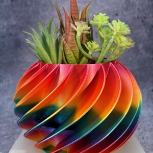 May include: A rainbow swirl planter with a variety of green succulents. The planter is made of a 3D printed material and has a glossy finish.