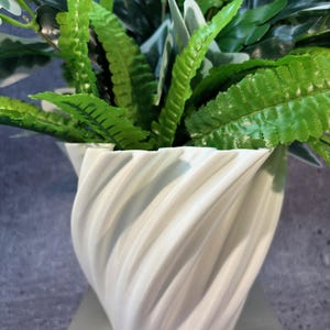 May include: White ceramic planter with a swirling, textured design. The planter is filled with green leafy plants.