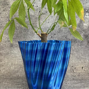 May include: A blue, wavy, 3D printed planter with a green leafy plant growing inside.