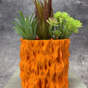 Pode incluir: Vaso de cerâmica texturizado laranja com três plantas suculentas artificiais. O vaso tem um design ondulado e orgânico.