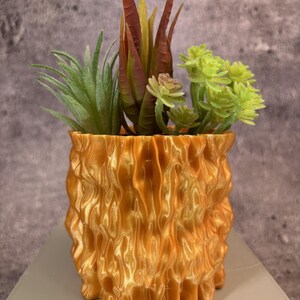 May include: A gold-coloured, textured ceramic planter with a variety of green and red succulents.
