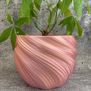 Może przedstawiać: Różowa doniczka w kształcie spirali z zieloną rośliną w środku. Doniczka wykonana jest z gładkiego, fakturowanego materiału i ma szeroki, okrągły otwór.