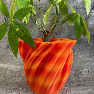Puede incluir: Una maceta de color naranja brillante en forma de espiral con una planta verde de hojas dentro. La maceta tiene una superficie texturizada y ondulada.