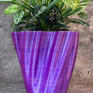 May include: A purple, wavy, textured, plastic plant pot with a green plant inside.