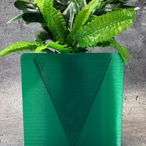 May include: A vibrant green planter with a V-shaped design, holding a mix of green and white leafy plants. The planter is a solid, square shape with a base. The plants have a variety of textures and shades of green.