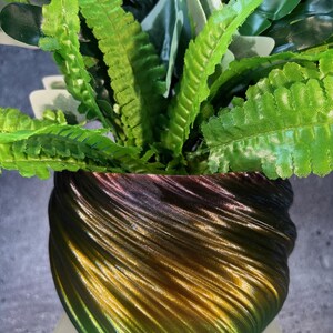 May include: A green, brown, and purple iridescent planter with a swirling pattern. The planter is filled with a green leafy plant.