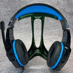 Op de afbeelding: Zwarte en blauwe gaming-headset met een gevoerde hoofdband en oorkussens. De headset staat op een standaard.