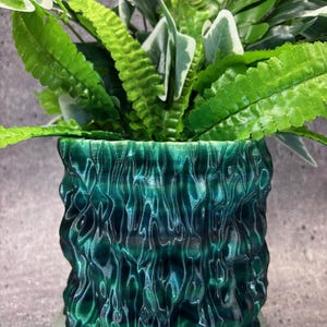 May include: A green and blue textured ceramic planter with a leafy green plant inside.