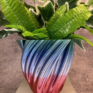 May include: A blue and pink ombre planter with a swirling, textured design. The planter is filled with green leafy plants.