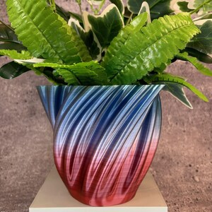 May include: A blue and red ombre swirl planter with a leafy green plant inside.
