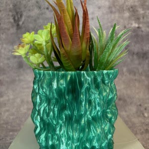 Può includere: Un vaso in ceramica verde testurizzato con una varietà di piante grasse. Il vaso ha un design ondulato e organico.