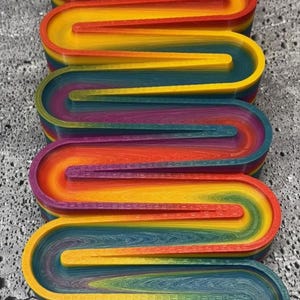May include: A colorful marble run toy with a rainbow gradient design. The toy features multiple levels with curved tracks and a collection tray filled with glass marbles. The tracks are in shades of purple, red, orange, yellow, green, and blue.