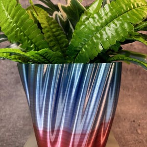 May include: A blue and red ombre planter with a wavy, textured design. The planter is filled with green leafy plants.