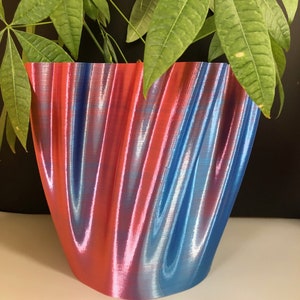 Op de afbeelding: Een blauwe en rode golvende keramische plantenpot met een glanzende afwerking. De pot is leeg.