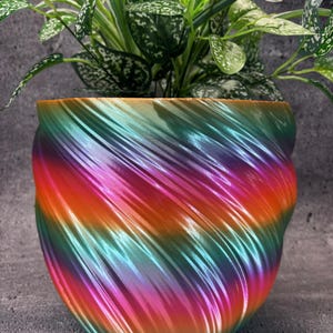 May include: A colorful, iridescent planter with a swirling pattern in shades of orange, pink, green, and blue. The planter is made of a smooth, glossy material.
