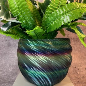 May include: A green iridescent planter with a swirling pattern, holding a leafy green plant.