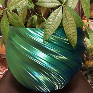 May include: A green and blue swirl planter with a green plant inside. The planter is made of a 3D printed material and has a shiny finish.