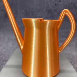 Puede incluir: Una regadera de plástico naranja brillante con un pico largo y un asa. La regadera tiene un acabado liso y brillante.