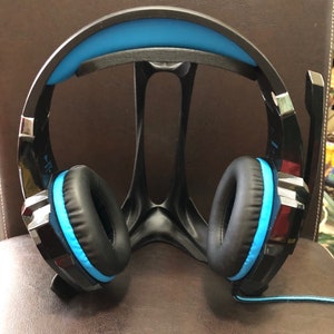 May include: Black gaming headset with blue accents. The headset is on a black stand.