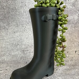 Puede incluir: Un macetero de bota de goma negra con una planta suculenta verde que crece desde la parte superior.