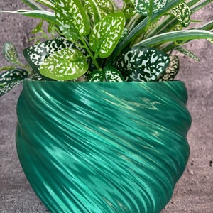 May include: A vibrant green, textured planter filled with lush, green and white spotted plants. The planter has a unique, swirling design. The plants have large, speckled leaves and long, slender leaves with white stripes. The background is a neutral gray.
