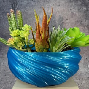 May include: A blue swirl planter with a variety of green and orange succulents. The planter is made of a smooth, shiny material.