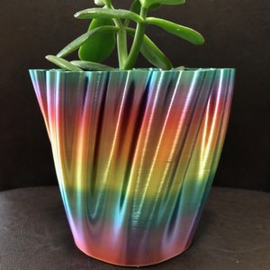 Puede incluir: Una maceta de cerámica de color arcoíris con un patrón de espiral que contiene una planta suculenta verde.