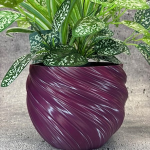 May include: A purple swirl planter with a green leafy plant inside. The planter is made of a smooth, textured material and has a unique, modern design.