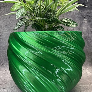 May include: A vibrant green plant pot with a glossy, spiralling, wave-like texture on its exterior surface. The pot contains a leafy plant with variegated green and white foliage that extends upwards from the centre of the container.