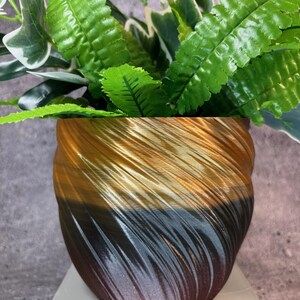 Può includere: Un vaso a spirale dorato, nero e marrone con una pianta verde al suo interno.
